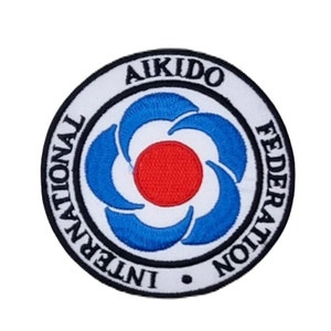 Peut inclure: Un écusson brodé blanc, bleu et rouge avec le texte "International Aikido Federation" et le mot "Aikido" dans un cercle noir.