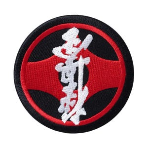 Puede incluir: Parche bordado redondo con fondo negro y círculo interior rojo. El parche presenta caracteres japoneses blancos en el centro. El diseño es un emblema audaz y contrastante.