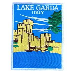 Op de afbeelding: Geborduurde patch met een geel kasteel met een blauw meer en groene bomen op de achtergrond. De tekst "LAKE GARDA ITALY" is in wit op een blauwe achtergrond geschreven.