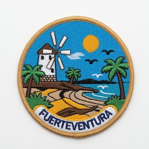 Könnte beinhalten: Runder, gestickter Aufnäher mit einer Küstenlandschaft mit Windmühle, Palmen und dem Text "FUERTEVENTURA". Der Aufnäher hat einen blauen Hintergrund mit einer gelben Sonne und Vögeln. Der Rand ist beige.