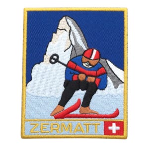 Op de afbeelding: Geborduurde patch met een skiër in rode en blauwe kleding, die een besneeuwde berg afdaalt. De patch heeft een blauwe achtergrond met het woord "ZERMATT" en een Zwitserse vlag.