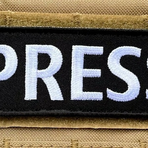Peut inclure: Un patch noir avec du texte brod&eacute; en blanc qui dit "PRESS".