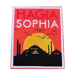Può includere: Una toppa ricamata con sfondo rosso e bordo bianco. La toppa presenta una silhouette della moschea di Santa Sofia a Istanbul, Turchia, con un sole giallo e uccelli nel cielo. Il testo "HAGIA SOPHIA" è ricamato in bianco sulla toppa.