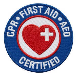 Könnte beinhalten: Ein kreisförmiger blauer Aufnäher mit weißem Text, der „CPR • FIRST AID • AED CERTIFIED“ lautet. In der Mitte befindet sich ein rotes Herz mit einem weißen Kreuz. Der Aufnäher ist wahrscheinlich für die Erste-Hilfe-Zertifizierung.