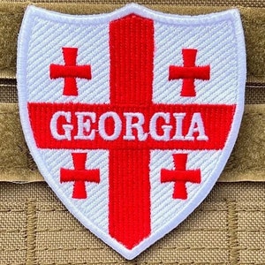 May include: A white and red embroidered patch in the shape of a shield. The patch features a red cross with four smaller red crosses and the word "GEORGIA" in white.