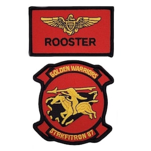 Può includere: Due toppe ricamate. La toppa superiore è rossa con un bordo nero e dice "ROOSTER" in testo nero. Sopra il testo c'è un aereo dorato con le ali e un emblema rosso, bianco e blu. La toppa inferiore è rossa con un bordo nero e dice "GOLDEN WARRIORS" in testo giallo attorno a un cerchio rosso. All'interno del cerchio c'è un'immagine nera e dorata di tre guerrieri a cavallo. Il testo "STRKFITRON 87" è in testo giallo sotto il cerchio.