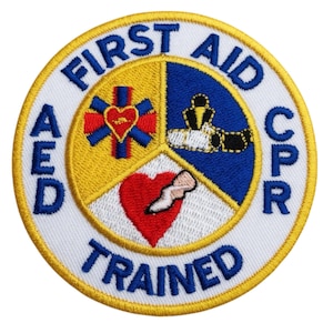 Op de afbeelding: Geborduurde ronde patch met de tekst "FIRST AID CPR TRAINED" in blauw. Het ontwerp heeft een segmentpatroon met een rood hart, een medisch symbool en een CPR-afbeelding. De patch heeft een witte achtergrond met een gele rand.