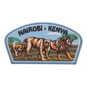 Könnte beinhalten: Gestickter Aufnäher mit einer Löwenfamilie, die über eine Wiese läuft. Der Aufnäher hat einen hellblauen Rand und Hintergrund mit dem Text "NAIROBI - KENYA" oben. Die Löwen sind orange und weiß.
