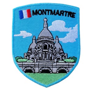 Puede incluir: Parche bordado con la basílica del Sacré-Cœur en Montmartre, París. El parche tiene un fondo azul claro con el texto "MONTMARTRE" y una bandera francesa. La basílica está representada en gris y blanco.