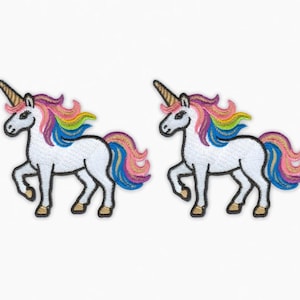 Op de afbeelding: Twee geborduurde eenhoornpatches. Elke witte eenhoorn heeft een gouden hoorn, een regenboogmanen en -staart en zwarte hoeven. De patches staan op een witte achtergrond.