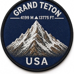 May include: A circular embroidered patch featuring a dark blue background with a detailed mountain peak in shades of brown and white. The text reads GRAND TETON, 4199 M, 13775 FT, and USA in white lettering. The patch has a thick black stitched border.