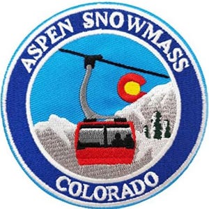 May include: Embroidered patch with the text "ASPEN SNOWMASS COLORADO" in a circular design. The patch shows a ski lift, a red ski lift car, a yellow and red sun, and white snow-capped mountains against a blue background.