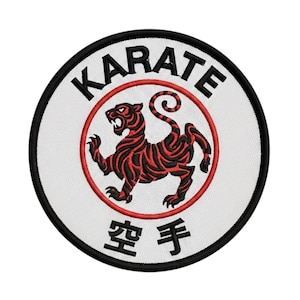 Pode incluir: Patch bordado com a palavra "KARATE" em preto, arqueada sobre um círculo vermelho. Dentro do círculo, um tigre vermelho e preto. Caracteres japoneses abaixo. Fundo branco, borda preta.