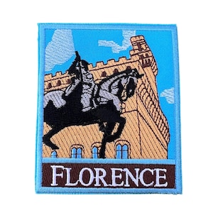Könnte beinhalten: Ein gestickter Aufnäher mit blauem Hintergrund, einem beigefarbenen Gebäude mit einem Turm, einem schwarzen Pferd mit einem Reiter und dem Wort "FLORENCE" in braunen Buchstaben.