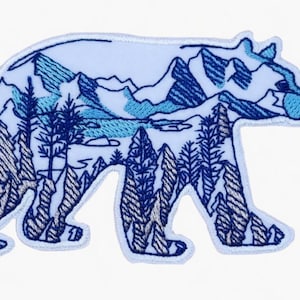 Peut inclure: Écusson brodé en forme d'ours, représentant un paysage de montagnes et de forêts. Le motif utilise des nuances de bleu et de blanc, avec des coutures détaillées créant le paysage. Idéal pour les vêtements ou accessoires.