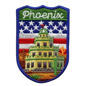 Puede incluir: Parche bordado con una imagen estilizada de un edificio con una cúpula, rodeado de cactus y un paisaje desértico. El parche tiene un borde azul y un fondo de bandera estadounidense rojo, blanco y azul. El texto "Phoenix" está bordado en blanco sobre un fondo verde en la parte superior del parche.