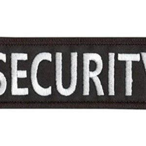 May include: A rectangular black patch with the word "SECURITY" embroidered in white block letters. The patch has a dark brown border and is likely designed to be sewn or attached to clothing or gear.