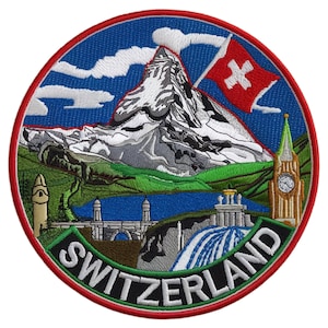 May include: Circular embroidered patch depicting a Swiss landscape. It shows a mountain, a Swiss flag, a lake, a waterfall, and a clock tower. The word "SWITZERLAND" is at the bottom. The design uses red, white, blue, green, and grey colours.
