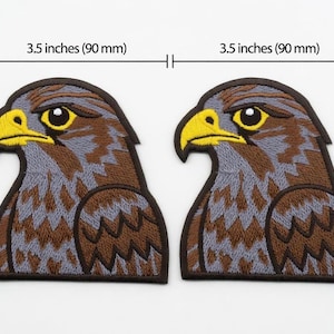 Pode incluir: Dois patches bordados com a cabeça de um falcão. Cada patch tem 90 mm de largura. O falcão tem um bico amarelo, penas castanhas e cinzentas e uma borda castanha escura. O olho é preto com um brilho branco.