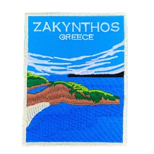 May include: An embroidered patch with a blue background and white text that reads "ZAKYNTHOS GREECE". The patch depicts a landscape with a green island and a blue sea.