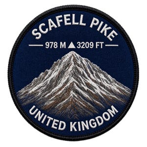 Op de afbeelding: Een ronde geborduurde patch met een donkerblauwe achtergrond en een illustratie van een berg in wit, grijs en bruin. De tekst SCAFELL PIKE staat bovenaan, 978 M 3209 FT in het midden en UNITED KINGDOM onderaan in witte draad.