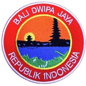 Può includere: Una toppa ricamata in rosso, bianco e blu con il testo "Bali Dwipa Jaya Republik Indonesia". La toppa presenta un'immagine stilizzata di un tempio con un tramonto alle sue spalle.