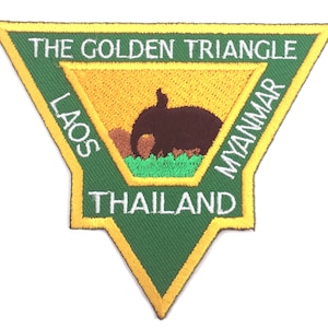 Może przedstawiać: Zielony trójkątny znaczek z żółtą obwódką. Znaczek zawiera napis "The Golden Triangle" u góry, "Laos" po lewej, "Myanmar" po prawej i "Tajlandia" na dole. W środku znaczka znajduje się brązowa sylwetka słonia.
