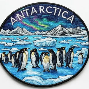 Può includere: Toppa ricamata circolare raffigurante l'Antartide. Il design include pinguini, iceberg, montagne e la scritta "ANTARCTICA". Lo sfondo mostra l'aurora boreale.