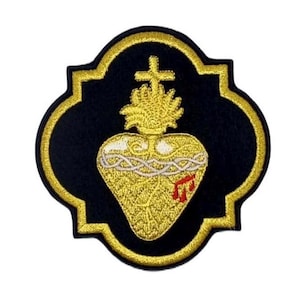 Könnte beinhalten: Gold gestickter Patch mit schwarzem Hintergrund, der ein stilisiertes Herz mit Dornenkrone, Kreuz und Flamme zeigt. Das Herz ist von einem goldenen Seil umgeben und hat rote Blutstropfen.