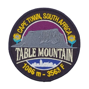Könnte beinhalten: Runder, gestickter Aufnäher mit dem Tafelberg in Kapstadt, Südafrika. Das Design enthält den Text "CAPE TOWN, SOUTH AFRICA" und "TABLE MOUNTAIN". Der Aufnäher zeigt auch die Höhe des Berges: 1086 m - 3563 F.