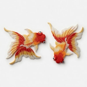 May include: Two embroidered goldfish patches. The fish have red heads, orange and yellow bodies, and white-tipped fins. The patches are detailed with black eyes and are set against a white background.
