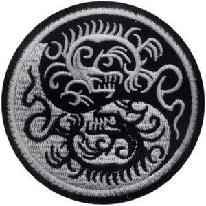 Può includere: Una toppa ricamata in bianco e nero con un design di drago stilizzato. Il drago è arrotolato in un cerchio, con la testa rivolta verso lo spettatore. La toppa è circolare e ha un bordo nero.