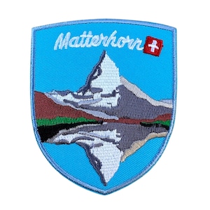 Peut inclure: Patch brodé représentant un ciel bleu avec un sommet de montagne, le Cervin, reflété dans un lac. Le texte "Matterhorn" et un drapeau suisse sont en haut du patch.