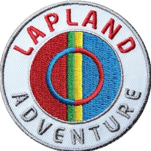 Peut inclure: Écusson brodé circulaire avec l'inscription "LAPLAND ADVENTURE" en rouge et gris. Le motif comprend un anneau rouge et bleu, et une bande verticale verte et jaune. Le patch est sur fond blanc.