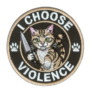 Op de afbeelding: Geborduurde patch met een cartoonkat die een mes vasthoudt. De kat is bruin en beige met zwarte strepen en groene ogen. De patch heeft de woorden "I CHOOSE VIOLENCE" in witte tekst rond de kat.