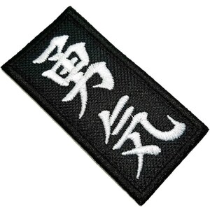 Pode incluir: Etiqueta bordada preta com caracteres japoneses brancos "戦場" que significa "campo de batalha".