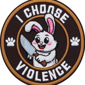 Peut inclure: Écusson brodé circulaire avec un lapin de dessin animé tenant un couteau. Le patch a un fond marron et une bordure beige. Le texte blanc dit "I CHOOSE VIOLENCE". Des empreintes de pattes flanquent le lapin.