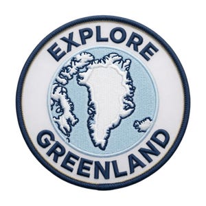 May include: A circular embroidered patch featuring a white map of Greenland centered on a light blue background. The text EXPLORE is arched across the top and GREENLAND is arched across the bottom in dark blue thread, all bordered by a dark blue edge.