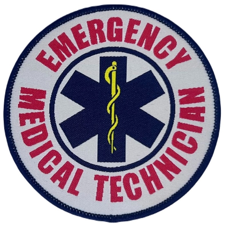 Op de afbeelding: Ronde witte patch met blauwe stiksels. In het midden van de patch bevindt zich een blauwe ster van het leven met een gele slang en staf. De tekst "EMERGENCY MEDICAL TECHNICIAN" staat in een rode cirkelvormige band rond de ster van het leven.