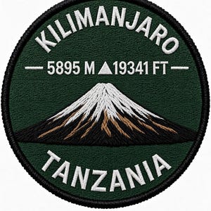 Op de afbeelding: Een ronde geborduurde patch met een donkergroene achtergrond en een witte berggrafiek. De tekst luidt KILIMANJARO, 5895 M, 19341 FT en TANZANIA in witte hoofdletters. De basis van de berg is zwart met witte en bruine accenten in het borduurwerk.