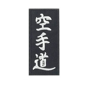 May include: A rectangular black patch with white embroidered Japanese characters. The characters are arranged vertically and read "Karate-Do". The patch has a simple, clean design, suitable for martial arts enthusiasts.