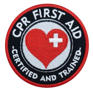 Könnte beinhalten: Runder Aufnäher mit dem Text "CPR FIRST AID CERTIFIED AND TRAINED" in weißer Schrift auf schwarzem Hintergrund. Ein rotes Herz mit weißem Kreuz befindet sich in der Mitte. Der Aufnäher hat einen roten Rand.