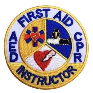 May include: A yellow, blue, and white embroidered patch with the text "FIRST AID CPR AED INSTRUCTOR". The patch features a red heart with a white bandage, a blue star of life with a red heart, and a blue figure with a white shirt and black belt.