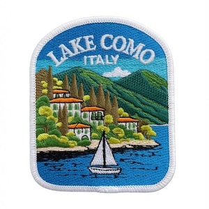 Könnte beinhalten: Ein gestickter Aufnäher mit einer Landschaft vom Comer See in Italien, mit weißem Text LAKE COMO ITALY oben. Das Design zeigt einen blauen See, ein weißes Segelboot, grüne Hügel, hohe Zypressen und weiße Gebäude mit orangefarbenen Dächern.