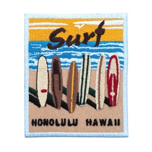 May include: Embroidered patch featuring a beach scene with surfboards. The word "Surf" is arched across the top, with "Honolulu Hawaii" at the bottom. The patch has a light blue border and depicts a sunset over the ocean.
