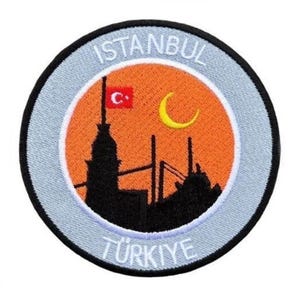 May include: A round, gray and white embroidered patch with the words "ISTANBUL" and "TÜRKIYE" in white. The patch features a silhouette of the skyline of Istanbul with a crescent moon and a red star.