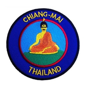 May include: A blue and red embroidered patch with the text "CHIANG-MAI THAILAND" around a yellow, orange, and green embroidered image of a meditating Buddha.