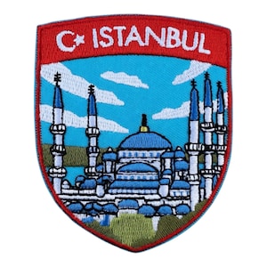 Op de afbeelding: Geborduurde patch met een schildontwerp. De patch toont de tekst "C* ISTANBUL" in wit op een rode achtergrond. Het toont een blauwe moskee met witte minaretten tegen een blauwe lucht met witte wolken. De patch heeft een rode rand.