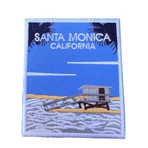 Könnte beinhalten: Gestickter Aufnäher mit blauem Hintergrund, der einen Rettungsschwimmerstand an einem Strand mit Palmen und dem Text "SANTA MONICA CALIFORNIA" zeigt.