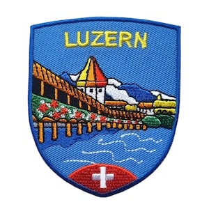May include: Embroidered patch with a blue shield design featuring the word "LUZERN" in yellow. The patch depicts a bridge, buildings, and mountains in various colours. A red and white Swiss cross is at the bottom.